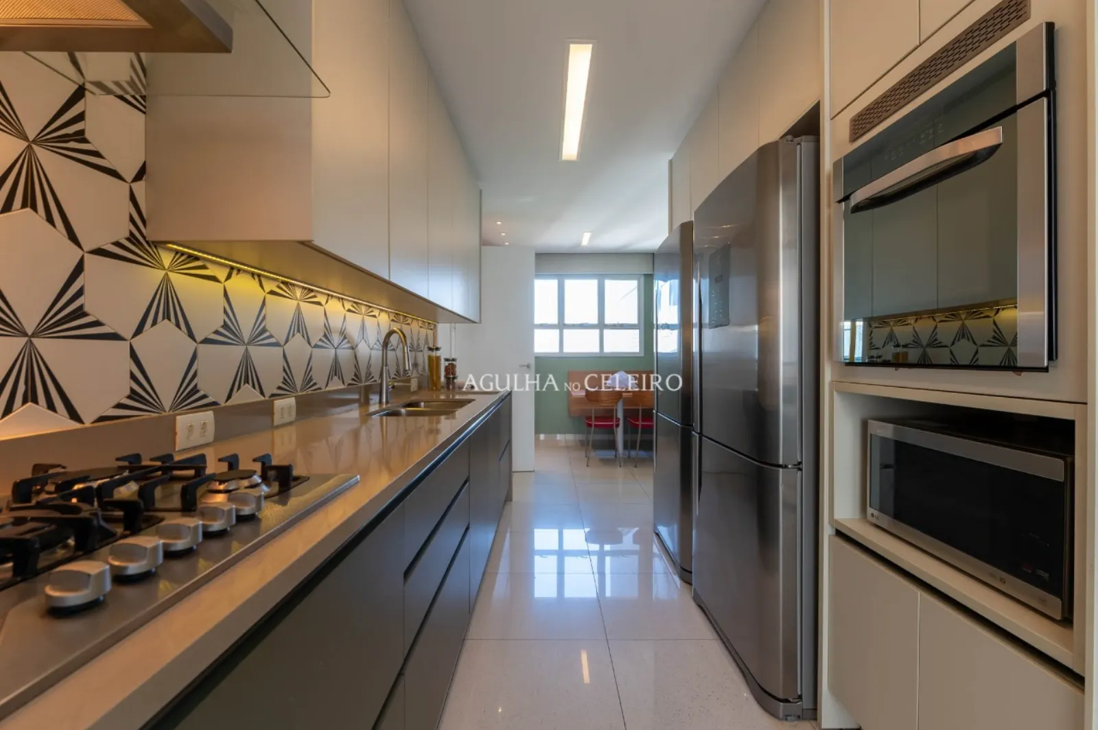 Cozinha com revestimento geométrico, eletrodomésticos de inox e marcenaria sob medida.